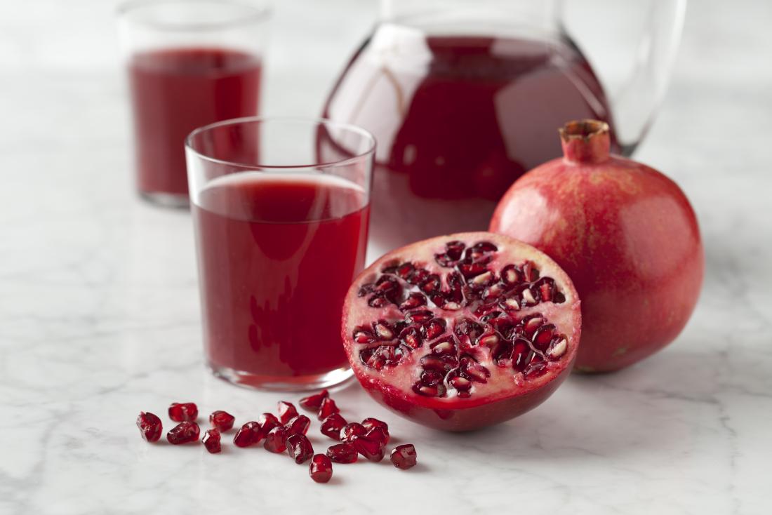 Metade a romã com sementes e suco de romã na superfície marmorizada.