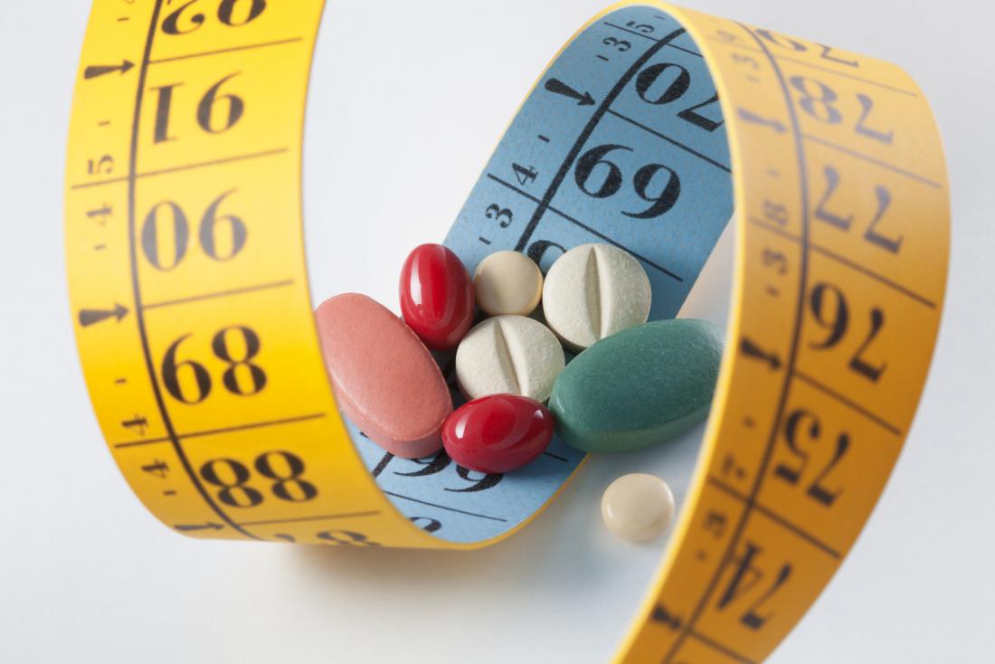 Perda de peso e pílulas dietéticas rodeadas por fita métrica.