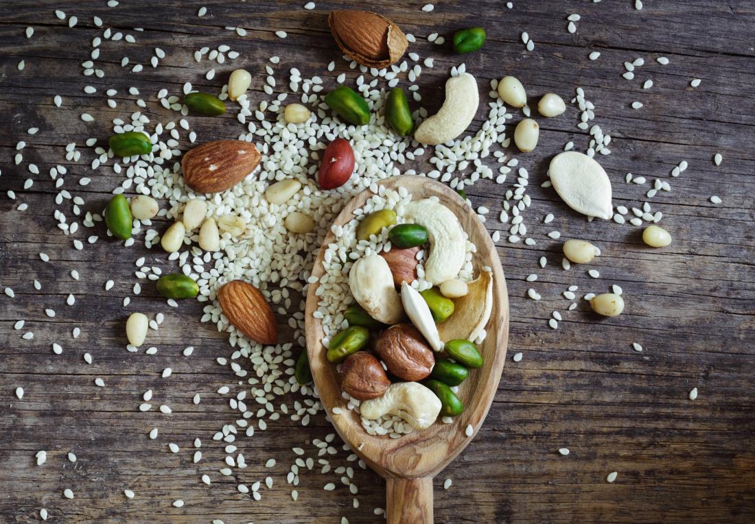 Mixed nuts and seeds on wooden spoon over table, including pine nuts, almonds, pistachios, and cashews.