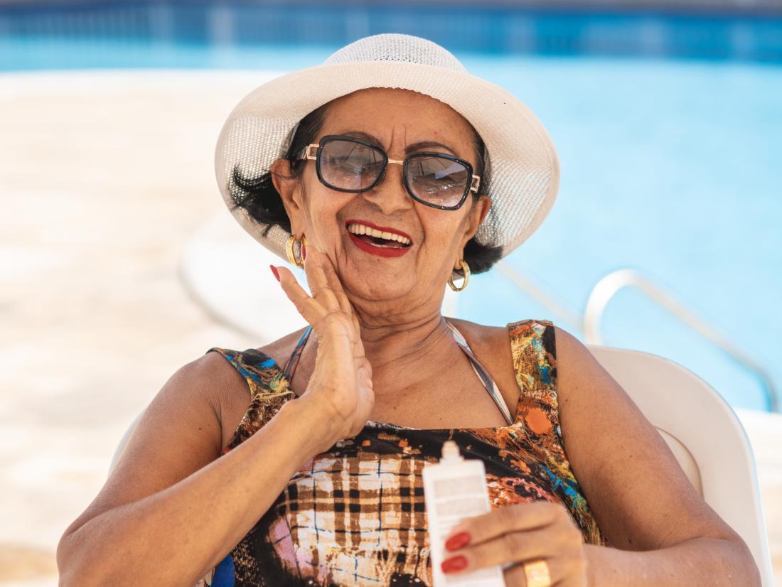 a senior lady applying sunscreen to her face. 