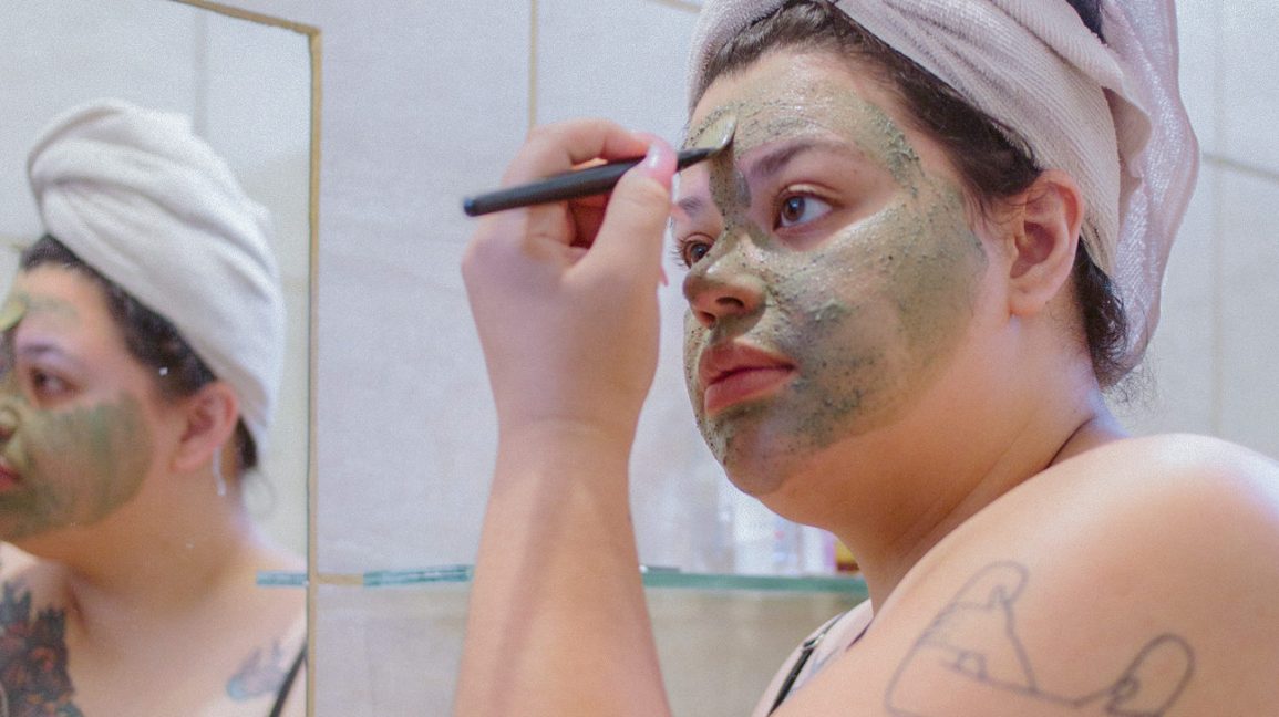 Mulher que aplica uma máscara protetora de chá verde com uma escova pequena. 