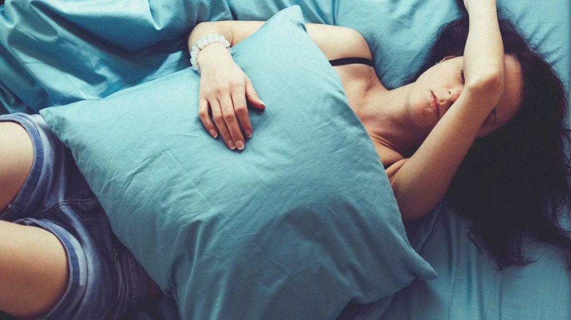 mulher de ressaca na cama com lençóis e travesseiro azuis
