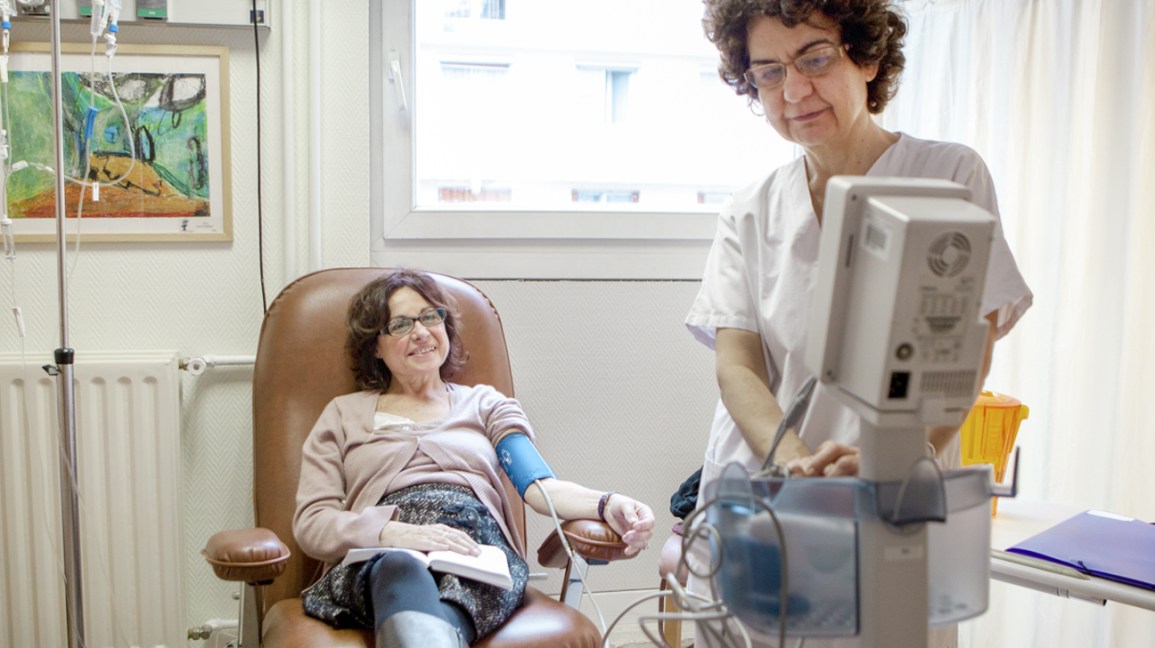 Quimioterapia vs. Radiação: Como eles diferem? 1 Uma mulher se senta em uma cadeira enquanto recebe uma infusão de quimioterapia em um ambiente médico.