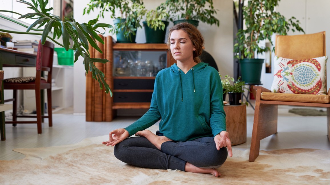 mulher sentada no chão meditando na frente de plantas
