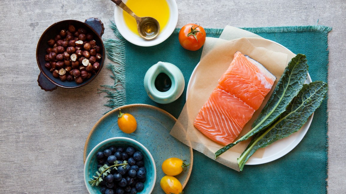 refeição saudável com alimentos integrais com salmão, couve, nozes, frutas e azeite