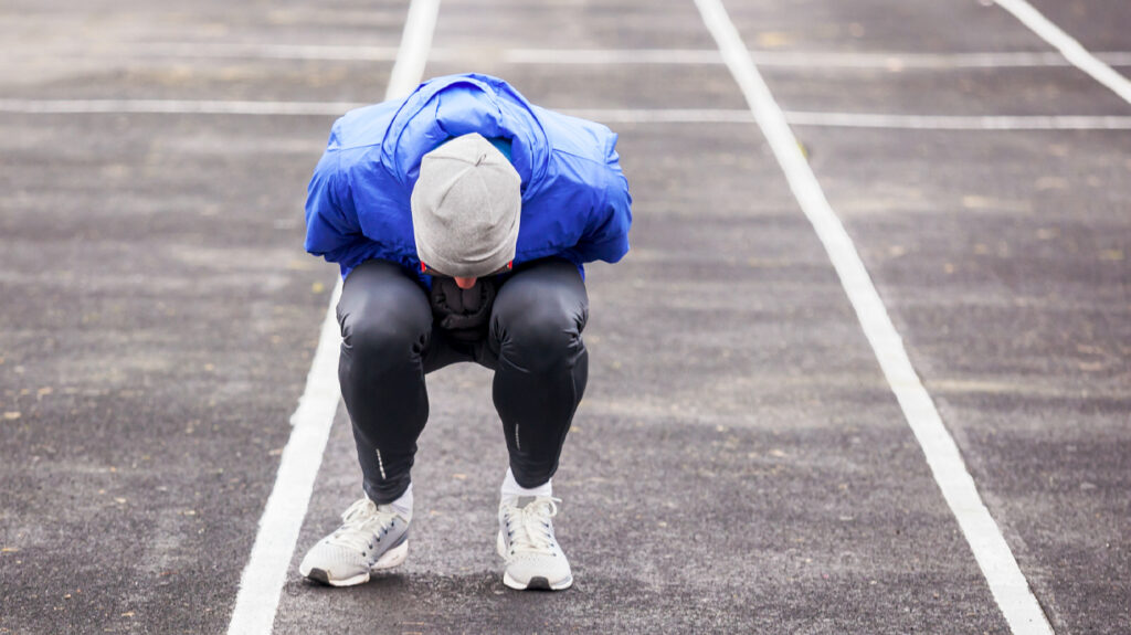 pessoa com uniforme de futebol na pista de corrida curvando-se e sentindo náuseas após o treino